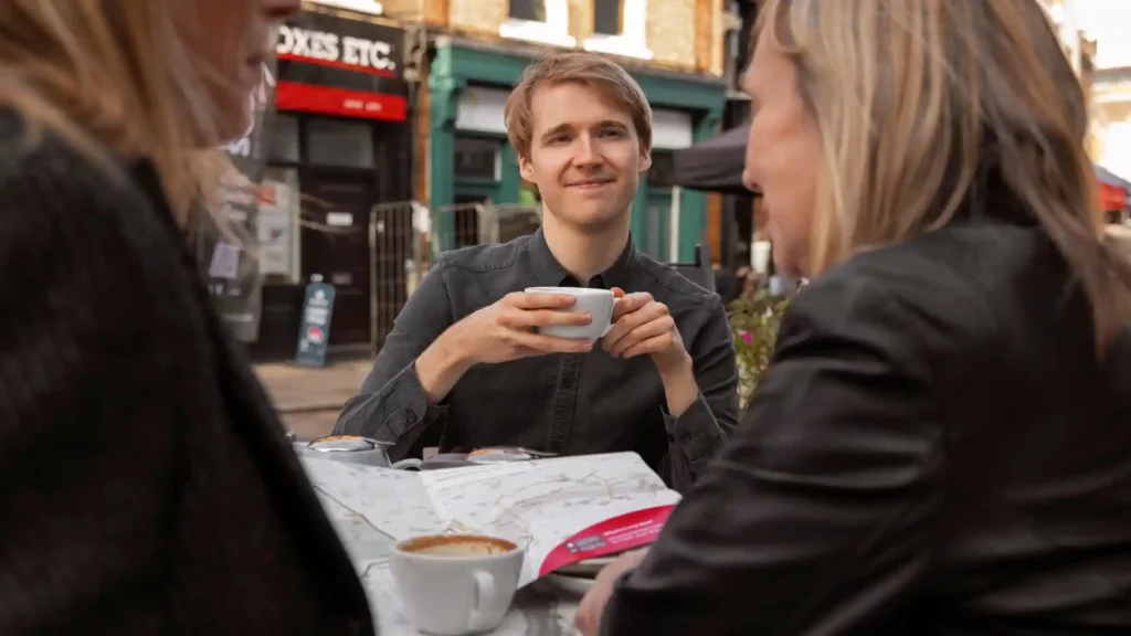 Ragazza con capelli biondi e camicia nera tiene in mano una tazza di caffè mentre cerca di capire una delle lingue locali che si parlano in Germania.