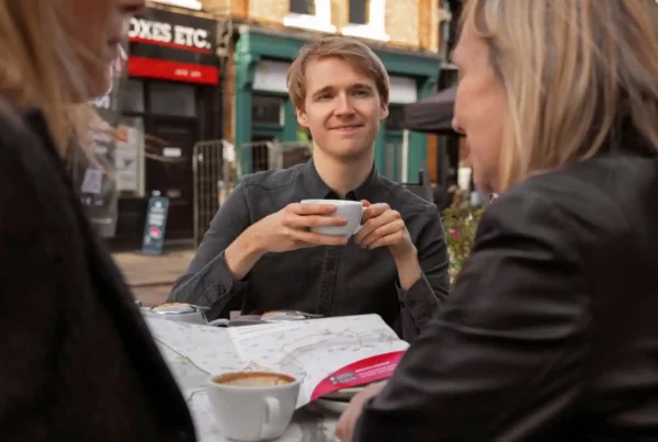 Ragazza con capelli biondi e camicia nera tiene in mano una tazza di caffè mentre cerca di capire una delle lingue locali che si parlano in Germania.