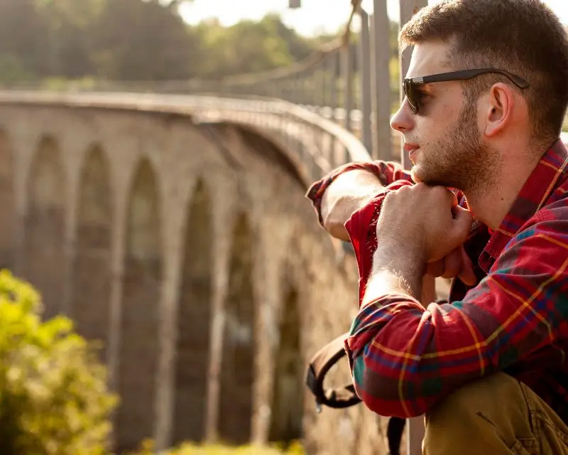 Ragazzo con occhiali da sole e camicia a quadri ammira il paesaggio pensando che ama molto la cultura tedesca
