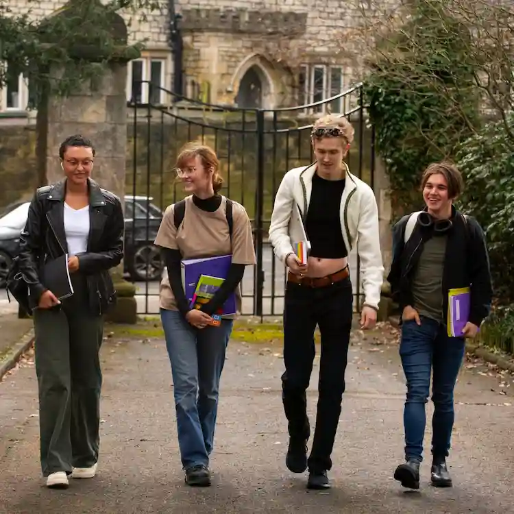 Quattro studenti sorridenti camminano insieme in un campus universitario storico, rappresentando il percorso accademico e la vita studentesca in un paese francofono.