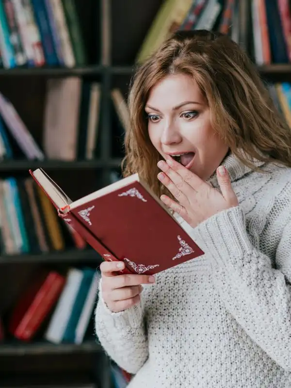 Ragazza stupita con un maglione bianco legge un libro che racconta tante curiosità sulla cultura tedesca