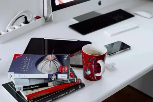 Libri per imparare lo spagnolo impilati su scrivania bianca accanto a tazza rossa e computer, pronti per lo studio