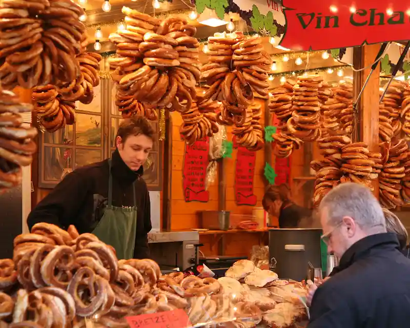 Feste francesi: bancarella tipica del mercatino di Natale di Strasburgo con pretzel giganti e insegne di vin chaud.