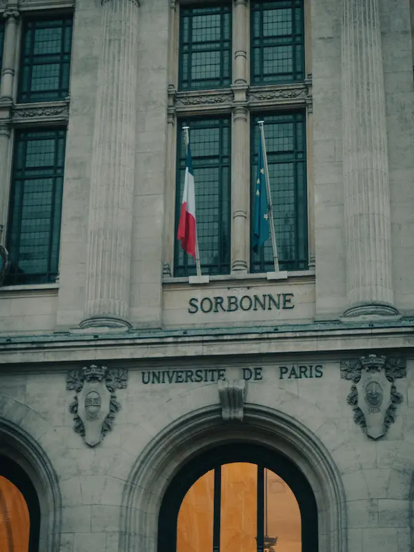 Facciata dell'Università della Sorbona a Parigi con bandiere francese ed europea, ideale per chi vuole studiare francese in un'università in Francia.
