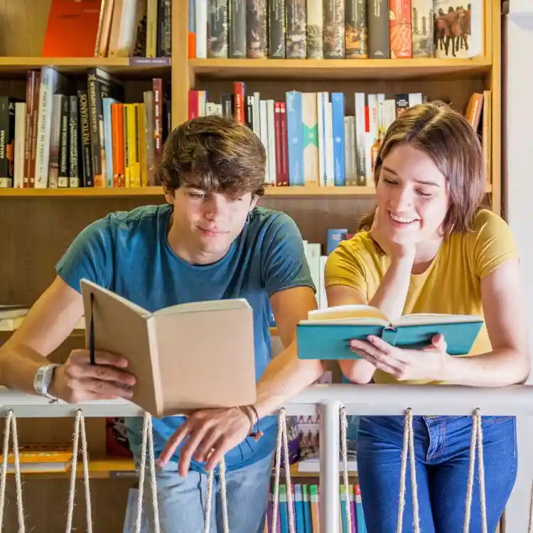 Ragazzo con una t-shirt blu e ragazza con una maglia gialla stanno imparando il tedesco dai libri in biblioetca.