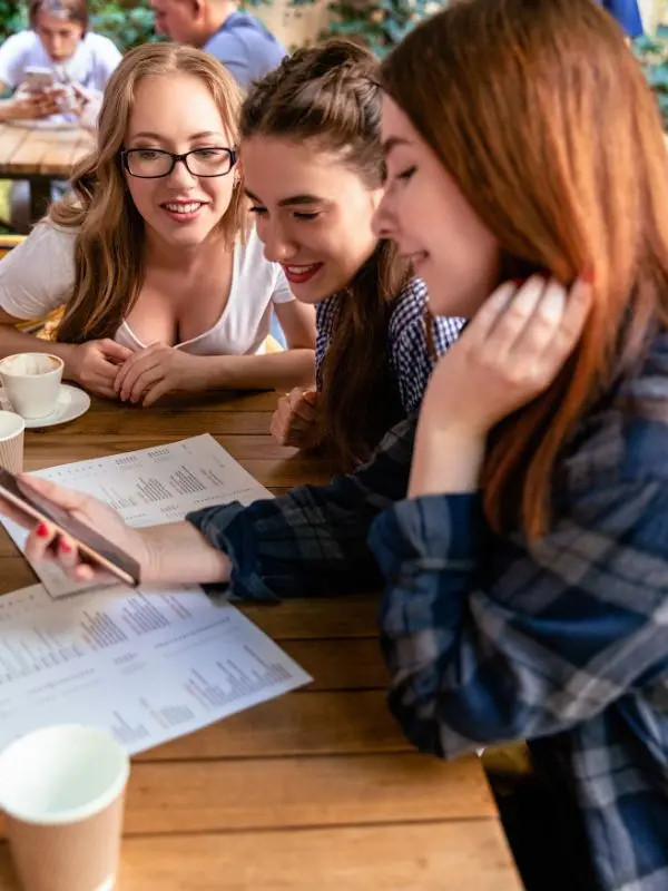 Tre amiche delle scuole superiori che sono anche compagne di scuola studiano il tedesco con un'app per imparare le lingue, prendendo appunti.