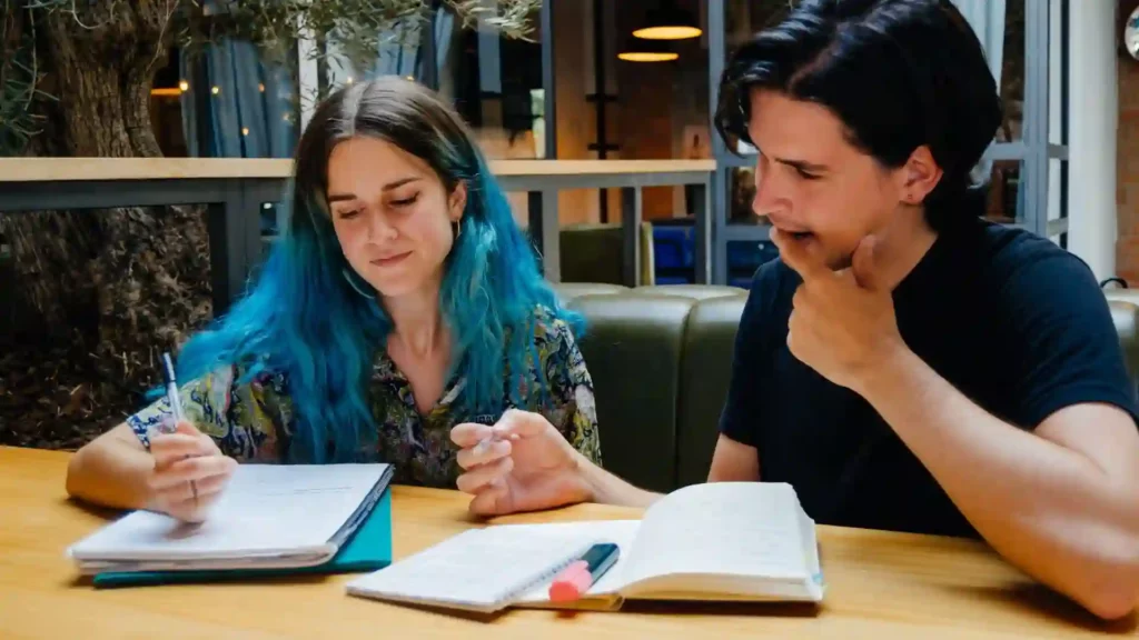 Ragazza con i capelli blu e ragazzo con maglietta nera sono in biblioteca e prendono appunti per imparare il tedesco.