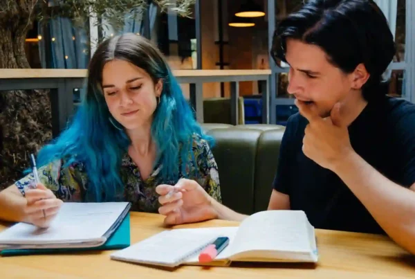 Ragazza con i capelli blu e ragazzo con maglietta nera sono in biblioteca e prendono appunti per imparare il tedesco.