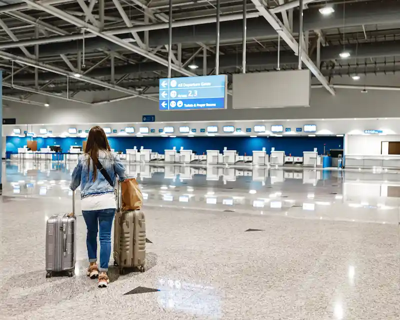 Una viaggiatrice si dirige ai banchi della consegna bagagli (bag drop) in aeroporto dopo il check-in online.