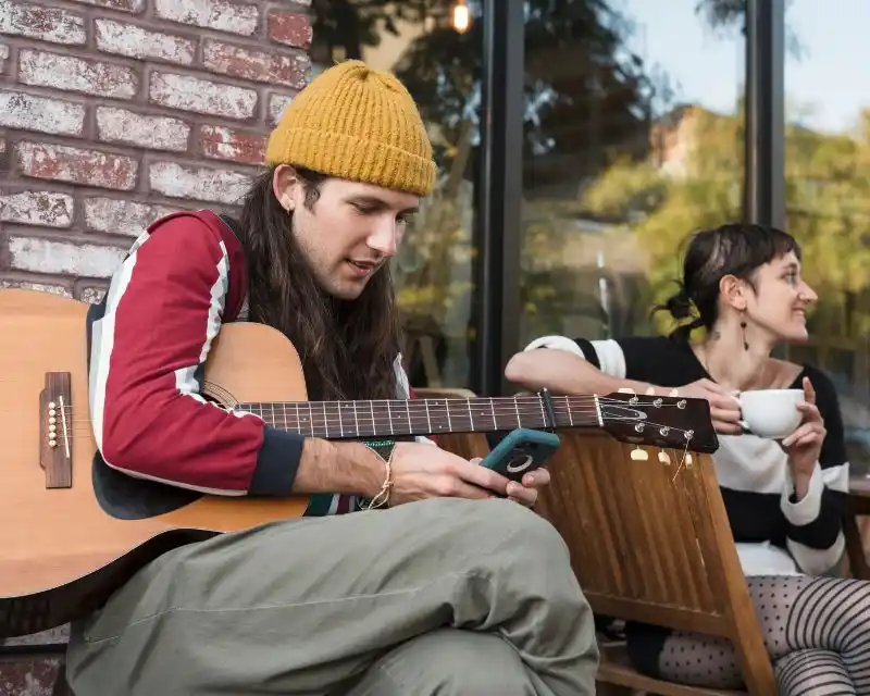 Un ragazzo con una chitarra e un cappellino giallo suona canzoni della tradizione tedesca in compagnia di un'amica.