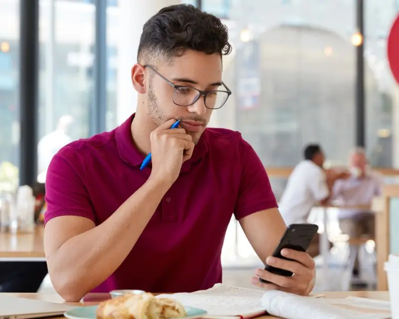 Ragazzo con gli occhiali, i capelli corti e una polo bordeaux studia il francese con il supporto di un'app.