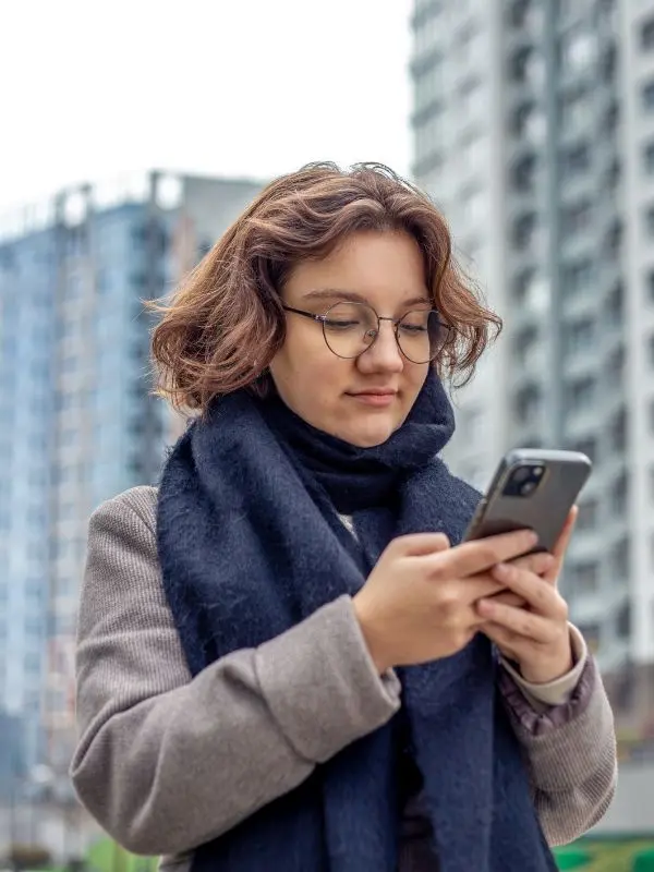 Ragazza con occhiali e sciarpa blu sta provando a usare un'app per imparare il francese.