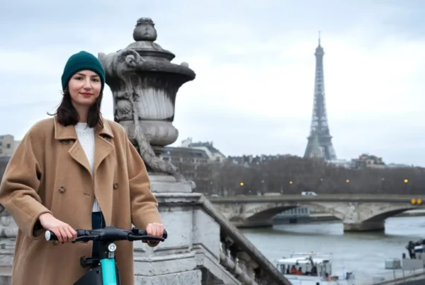 Ragazza con cappotto beige gira sul monopattino a Parigi alla scoperta delle curiosità sulla Francia.