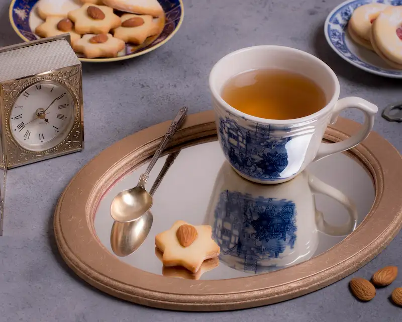 Tazza di tè con biscotti alle mandorle e un orologio vintage, simboli della tradizione inglese del tè.