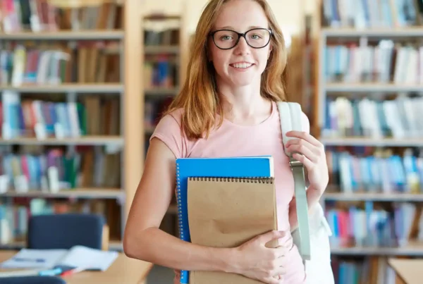 Studentessa con libri e zaino in una biblioteca, pronta a imparare l'inglese