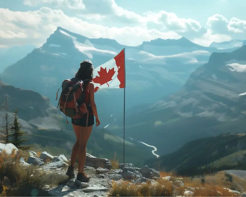 Ragazza con abbigliamento da trekking sta in piedi accanto alla bandiera canadese e ammira il paesaggio montuoso e alberato di uno degli Stati del Canada.