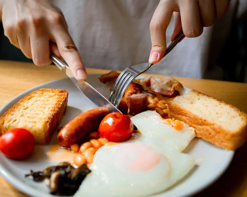 Primo piano di una Full English Breakfast con uova, salsiccia e fagioli, tipica delle tradizioni culinarie inglesi.