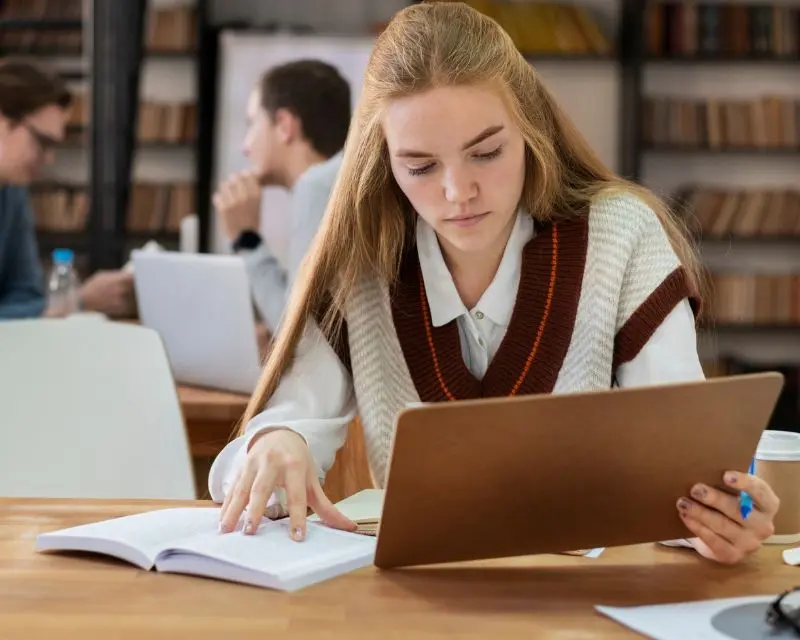 Ragazza con i capelli biondi e una camicia bianca sta studiando inglese online con il supporto del suo tablet.