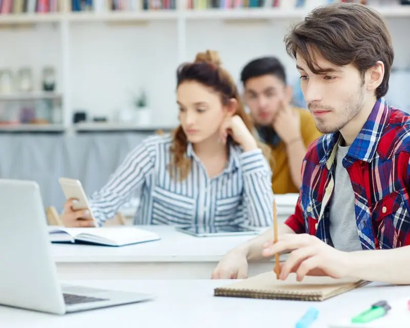 Ragazzo con camicia a quadri e capelli castani studia l'inglese online in aula studio.