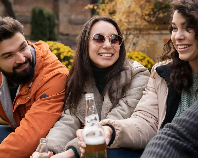 Ragazza con capelli lisci e occhiali da sole parla irlandese con due amici inglesi.