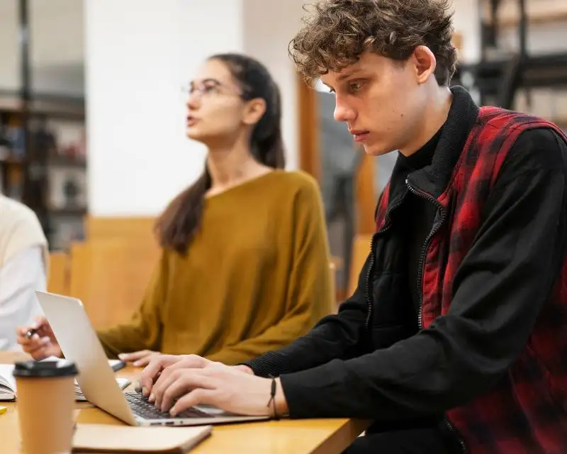 Ragazzo con capelli ricci e camicia nera cerca online un insegnante privato per imparare l'inglese da casa.