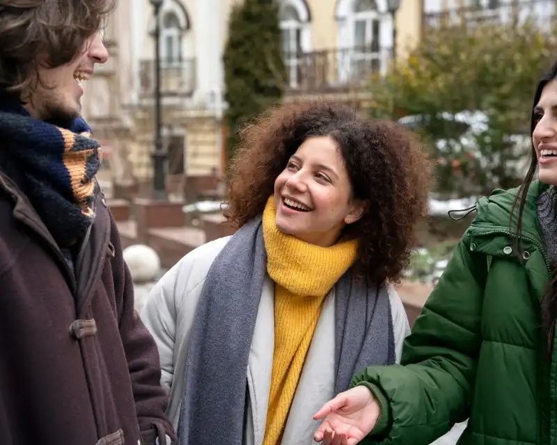 Ragazza con capelli ricci e maglione giallo parla irlandese con un amico con i capelli lisci lunghi e un'amica con il giubbotto verde.