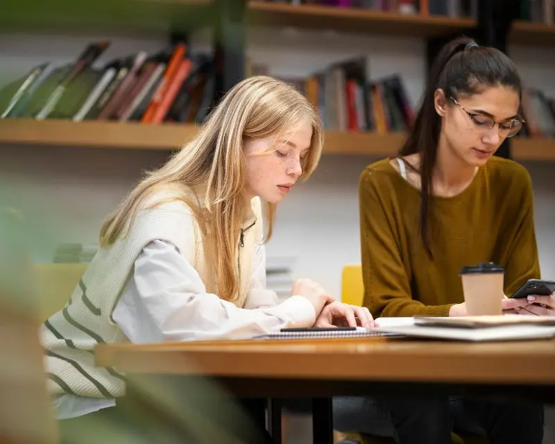 Due amiche studentesse sono in biblioteca per imparare insieme l'elenco di alcuni parole difficili da pronunciare in inglese.