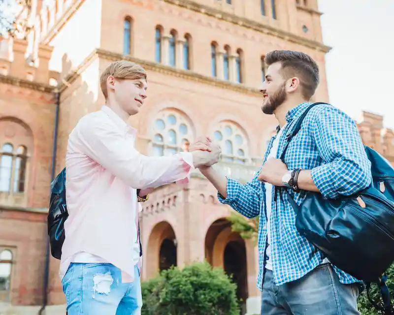 Due studenti universitari con zaino in spalla si salutano davanti a un edificio universitario