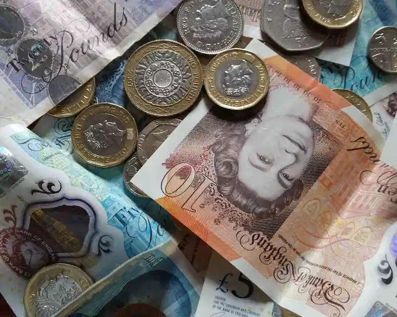 Banconote e monete con il volto della Regina Elisabetta II, un dettaglio ravvicinato che mostra il simbolo della sterlina inglese e il conio della moneta inglese.