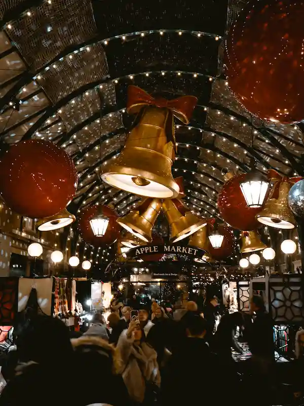 L'Apple Market di Covent Garden a Londra addobbato per il Natale, con campane dorate e luci festive tra la folla