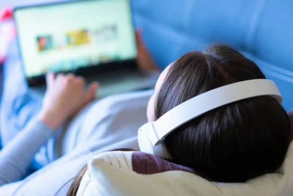 Ragazza sdraiata sul divano con le cuffie mentre guarda sul laptop i cartoni animati per imparare l'inglese