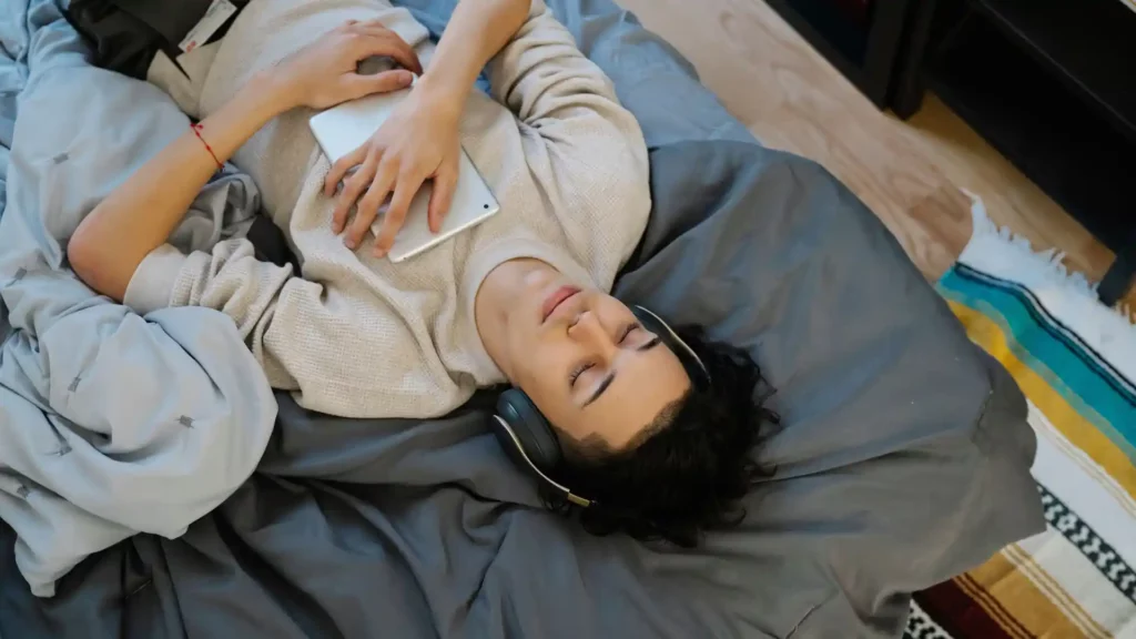 Ragazzo che dorme con le cuffie e un tablet sul petto mentre cerca di imparare l'inglese dormendo