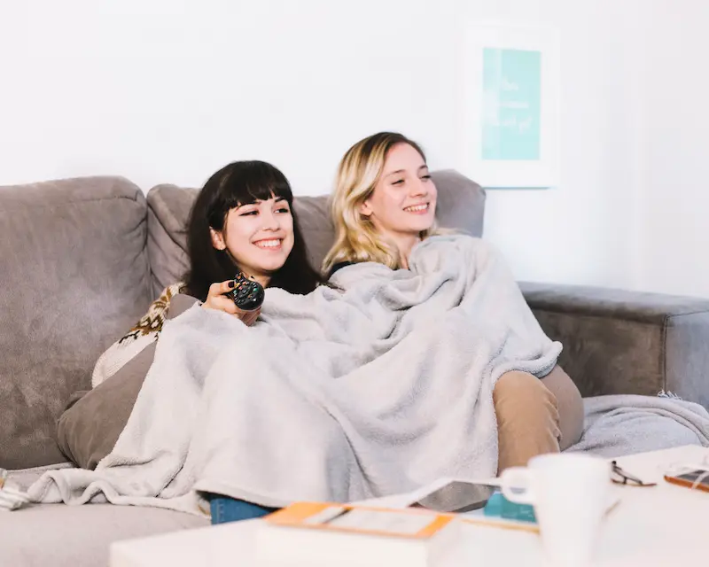 Due amiche sorridenti sul divano che guardano cartoni animati per imparare l'inglese