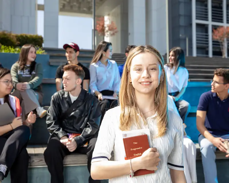 Studentessa sorridente con un libro di inglese tra un gruppo di studenti internazionali durante uno scambio all'estero