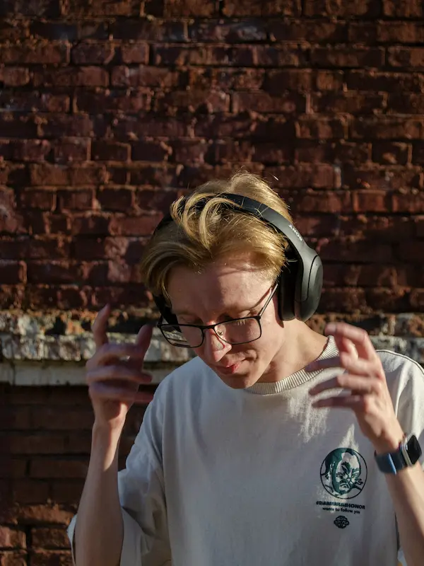 Ragazzo con cuffie e occhiali concentrato mentre ascolta musica, muovendo le mani a ritmo, per allenare l'ascolto attivo in inglese