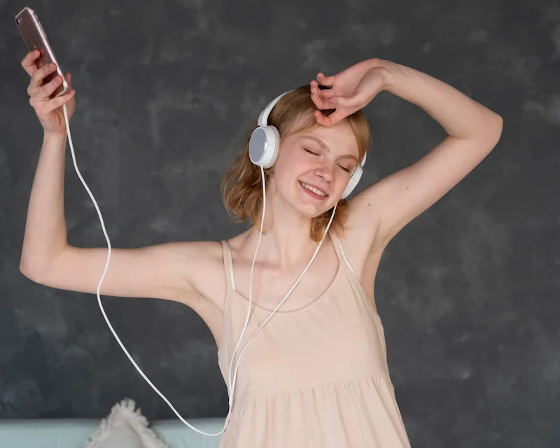 Ragazza sorridente balla con le cuffie mentre ascolta canzoni in inglese dallo smartphone, per imparare la lingua divertendosi